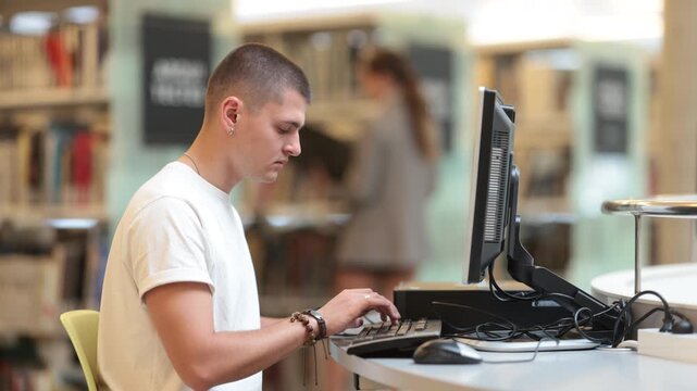 In reading room, guy student works at computer, searches for information online, checks and analyzes public data, student creates essay and completes homework, study for class assignment
