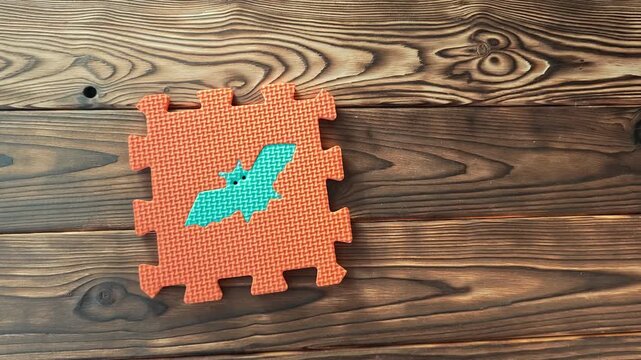 Hands put together puzzle pieces in a bright orange and blue design indoors, bat