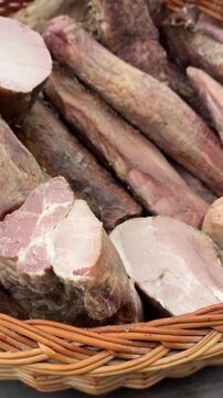 Wicker basket full of smoked meats pork ribs balyk assortment rustic meat display closeup