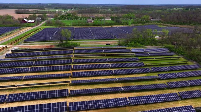 Aerial view of a vast solar panel array with symmetrical rows reflecting sunlight, amidst green fields, Lebanon, Ohio, United States.