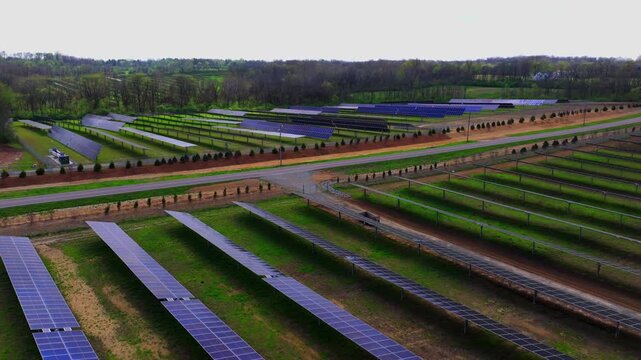 Aerial view of rows of solar panels contrasting with vibrant green grass and a backdrop of lush trees, creating a harmonious blend of technology and nature, Lebanon, Ohio, United States.