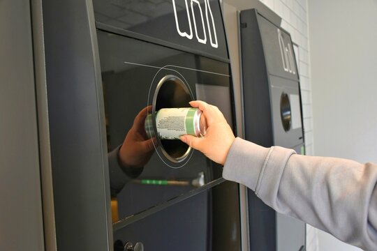 Returning empty cans to a supermarket recycling machine to reduce waste and reuse aluminum. A woman throws an aluminum can into a recycling machine.