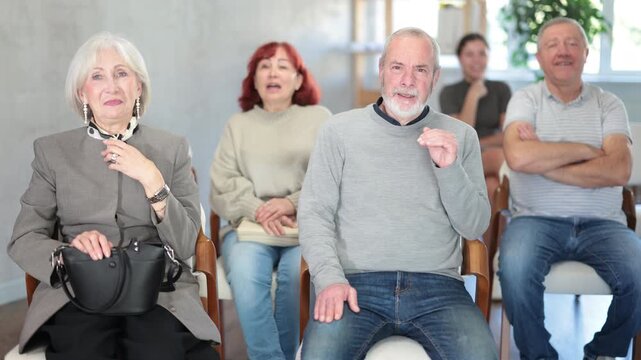 Cheerful and sociable group of students of different ages sitting on chairs, listening lecture and laughing in light lecture hall