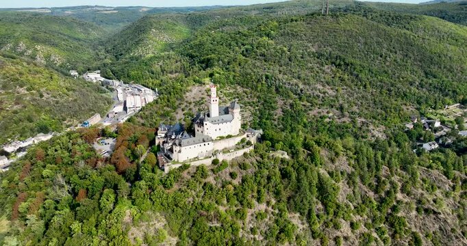 Aerial view of Marksburg castle standing atop a hill surrounded by lush green trees and buildings with a clear blue sky, Braubach, Germany.