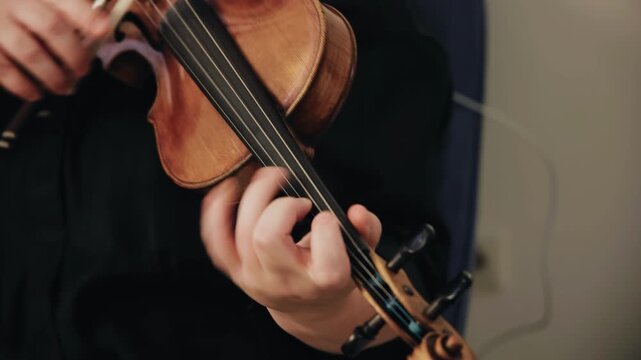 A violinist plays the violin. His hands clamp the strings and move the bow. Close-up shooting