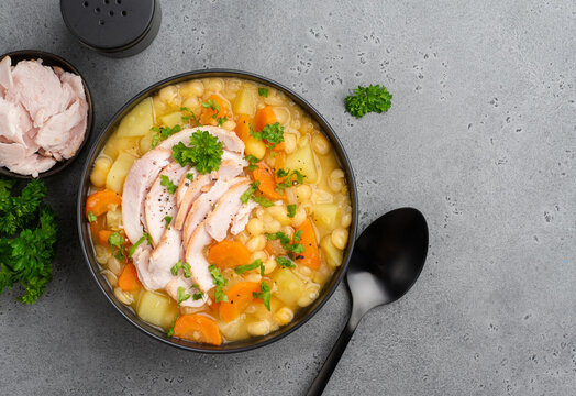 Pea soup with smoked chicken breast (fat free poultry meat). Healthy dinner or lunch full of fiber and proteins. Healthy eating concept. Soup in black bowl on dark grey table. Closeup. Copy space