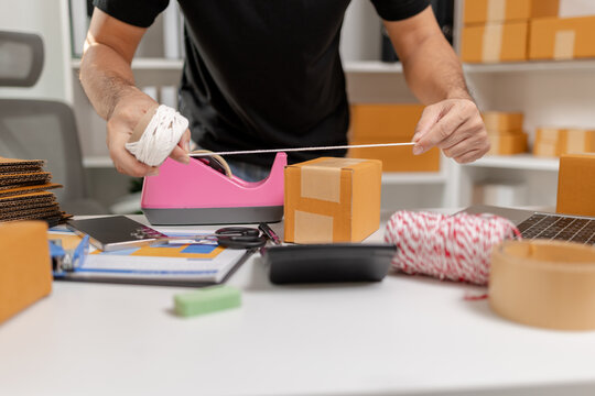 Small business owner tying parcel with string while preparing package for delivery, organizing shipping process and handling ecommerce orders, representing logistics and packaging workflow.