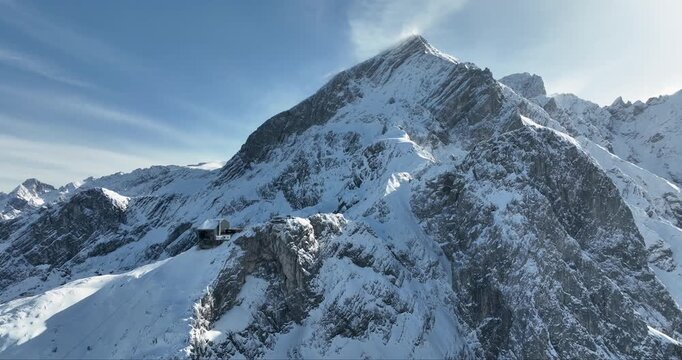 Aerial view of the snow-covered Zugspitze mountain peak, a majestic building clings to the mountainside, Garmisch-Partenkirchen, Bavaria, Germany.