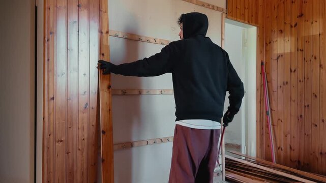 Timelapse footage of a worker dismantling wooden wall cladding using a crowbar during home renovation. Interior demolition scene with exposed wall structure and stacked boards.