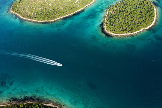 Aerial view of a lone boat slicing through the deep blue waters between verdant islands, creating a stark contrast with the turquoise shallows, Omis, Split-Dalmatia County, Croatia.