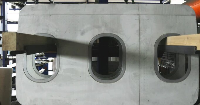 Aircraft fuselage panel with three window cutouts mounted on a rack in a workshop