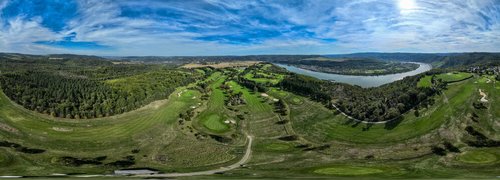 Aerial view of lush green golf course winding through rolling hills, reflecting the blue sky above, alongside the tranquil river, Boppard, Germany.