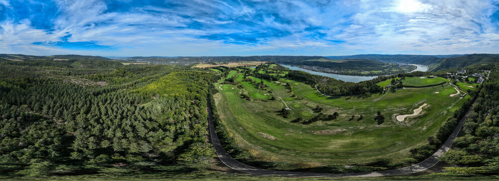 Aerial view of lush green golf course juxtaposed with dense forests and the winding river under a bright sky, Golfclub Jakobsberg, Germany.