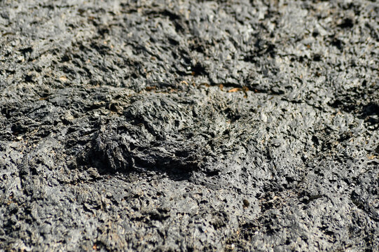 Close-up top view of a dark porous volcanic lava rock surface in Lanzarote. The texture shows cooled basaltic formations with irregular patterns.