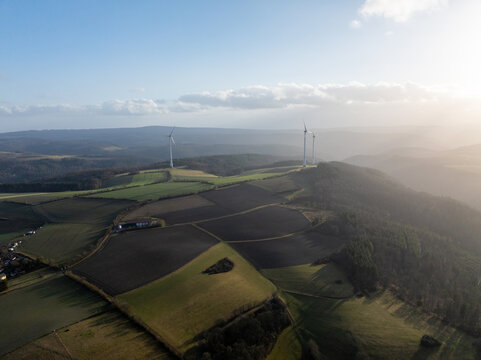 Aerial view of wind turbines standing tall against the horizon with agricultural fields and forests, Springen, Germany.
