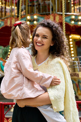 Fototapeta premium Joyful moments between a young mother and her daughter at a delightful amusement park setting