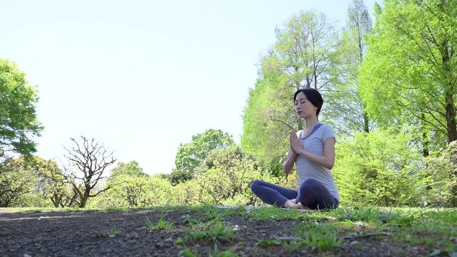 新緑の森や公園の屋外でヨガをする女性、瞑想と健康的ライフスタイル、リラックスとマインドフルネスイメージ　合掌のポーズ、アンジャリ・ムドラ　目を閉じる横顔の動画