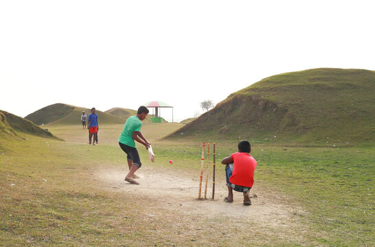 Sunamganj, Bangladesh - 26 January 2019: View of a cricket match unfolds on the grassy plain, with players poised against the backdrop of small, undulating hills.