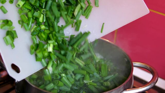 Adding chopped green onions to boiling water red kitchen stove closeup cooking process