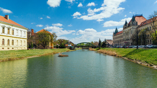 Aerial view of the tranquil Begej River flowing beneath a green bridge, framed by historic buildings under a bright sky, Zrenjanin, Vojvodina, Serbia.