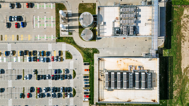 Aerial view of orderly parked cars contrast with the geometric precision of industrial buildings under the watchful eye of cylindrical tanks, Becej, Vojvodina, Serbia.
