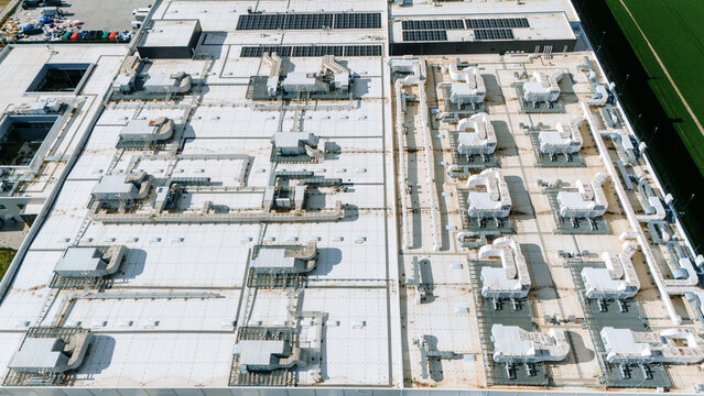 Aerial view of a stark white rooftop adorned with intricate HVAC systems and solar panels under the sun, creating a mesmerizing geometric landscape, Becej, Vojvodina, Serbia.