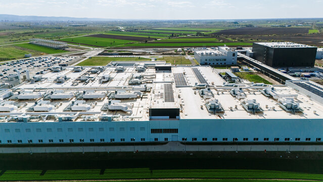 Aerial view of the sprawling industrial complex casting long shadows under the vast sky, contrasting sharply with the distant patchwork fields, Becej, Vojvodina, Serbia.