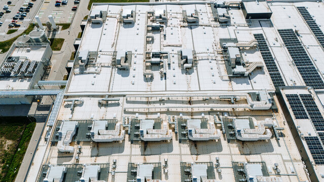Aerial view of the flat, white roof with multiple industrial ventilation systems and solar panels creating a geometric landscape, Becej, Vojvodina, Serbia.