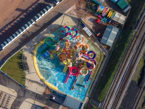 Aerial view of a vibrant waterpark with twisting slides and colorful structures, juxtaposed against the dull tones of the surrounding buildings, Paignton, England, United Kingdom.