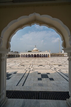 View of ornate marble patterns leading the eye to a distant mosque with a white dome under a soft sky, framed by an arched entrance, Nankana Sahib, Punjab, Pakistan.