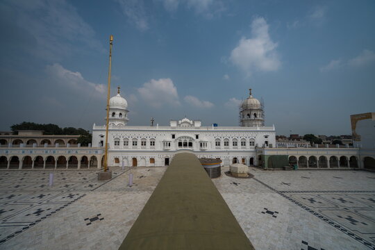 View of a gleaming white temple complex under a vast blue sky, its intricate architecture reflecting centuries of history and devotion, Nankana Sahib, Punjab, Pakistan.