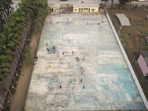 Aerial view of people scattered across a large court surface, bordered by lush trees and buildings, creating a vibrant scene, Lagos, Lagos, Nigeria.