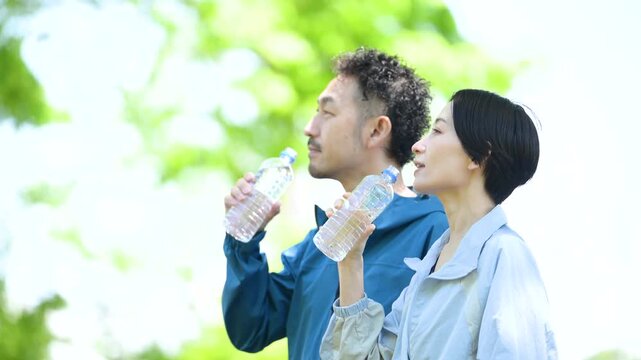 新緑の屋外でスポーツの合間に水分補給、ペットボトルの水を飲む夫婦の動画