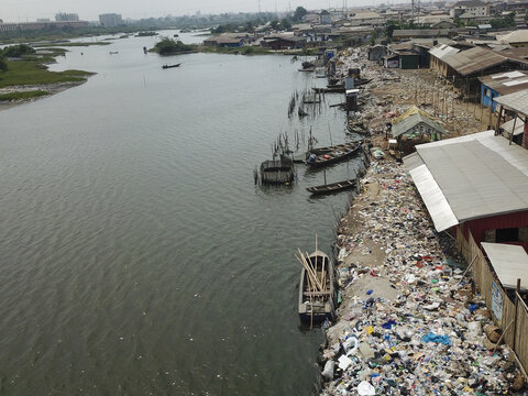 Aerial view of a riverbank littered with waste beside wooden shacks and boats in a low-income area, Oworonshoki, Lagos, Nigeria.