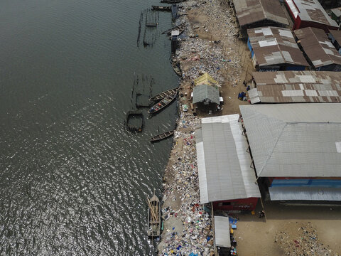 Aerial view of the stark contrast between the dark, rippling water and the chaotic, debris-strewn shoreline, Oworonshoki, Lagos, Nigeria.
