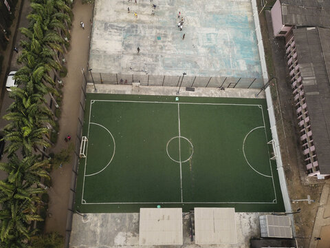 Aerial view of lush green soccer field contrasting with the faded blue basketball court, palm trees lining the periphery, Oworonshoki, Lagos, Nigeria.