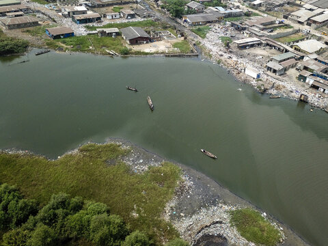 Aerial view of boats sailing on the murky water near the shoreline, where green vegetation meets urban sprawl, Oworonshoki, Lagos, Nigeria.