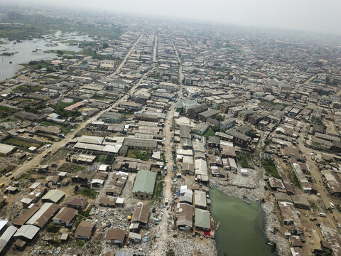Aerial view of a sprawling cityscape reveals dense buildings interspersed with waterways, creating a textured tapestry under a hazy sky, Oworonshoki, Lagos, Nigeria.