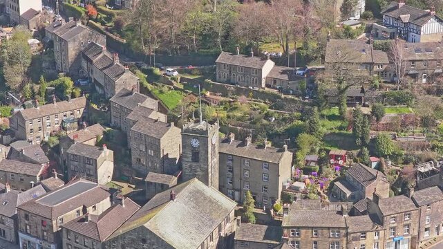 St John the Baptist Church and adjacent clock tower in Holmfirth Holme Valley Kirklees West Yorkshire England with sandstone architecture and terraced hillside gardens, drone ascending close up