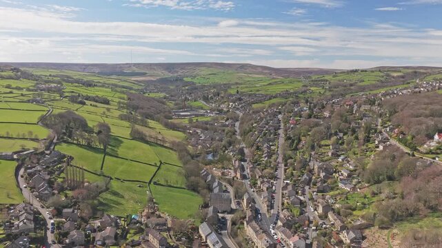 Holmfirth in Holme Valley West Yorkshire England with River Holme running through valley town surrounded by Pennine hills, pasture fields and dry stone walls, drone pullback shot