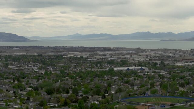 Pleasant Grove in Utah United States within Utah Valley with residential area extending toward Utah Lake and Lake Mountains across basin floor under stratocumulus clouds in early spring, forward glide