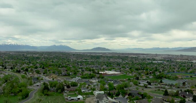 Pleasant Grove in Utah Valley, USA with residential grid spreading across the basin toward Utah Lake to the west and the Wasatch Range rising in the distance, under overcast sky drone forward flyover 