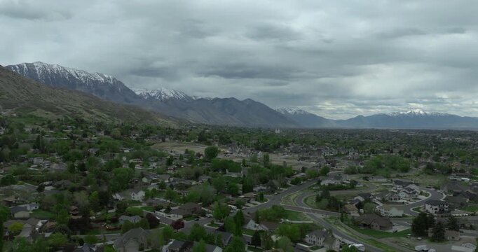 Pleasant Grove within Utah Valley showing residential grid toward Utah Lake and Lindon Temple with Wasatch Range and Mount Timpanogos Wasatch Range rising, stratocumulus cloud deck drone forward glide