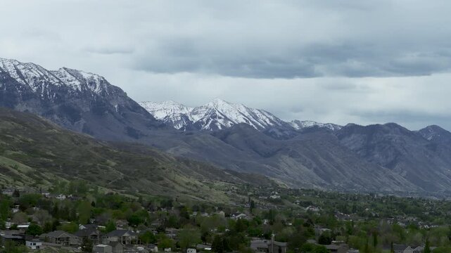 Lindon Orem and Provo in Utah Valley United States beneath Wasatch Range and Mount Timpanogos with residential areas on alluvial plain under spring snowpack, drone sliding lateral pan right and reveal