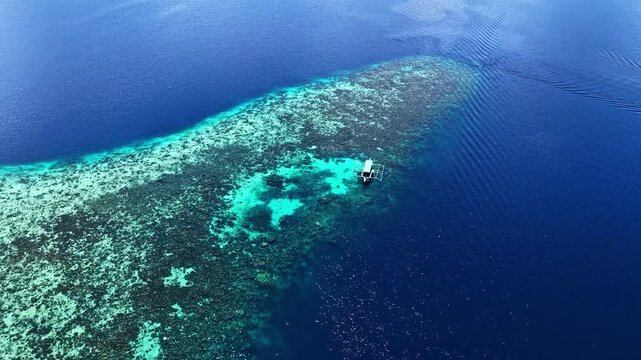 A single boat floats above a vibrant coral reef surrounded by deep blue waters, creating a striking contrast. charter dive boat. drone
