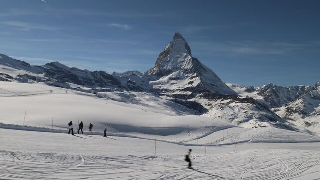 People skiing in Zermatt ski resort below Matterhorn, establishing wide view.