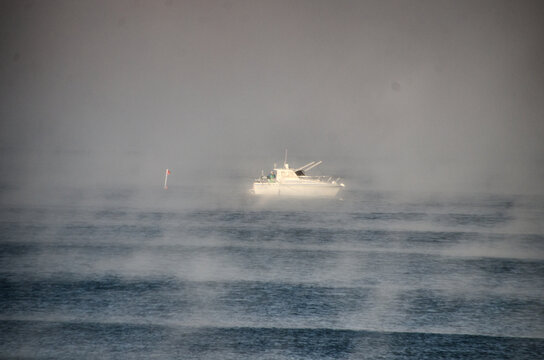 View of a white boat cuts through the misty, moody waters, a lone buoy marking its territory in the serene, yet foreboding seascape, Hossegor, France.