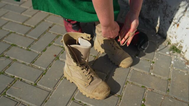 Boots tactical lacing woman in green dress putting on tan combat boots on a paved outdoor sidewalk