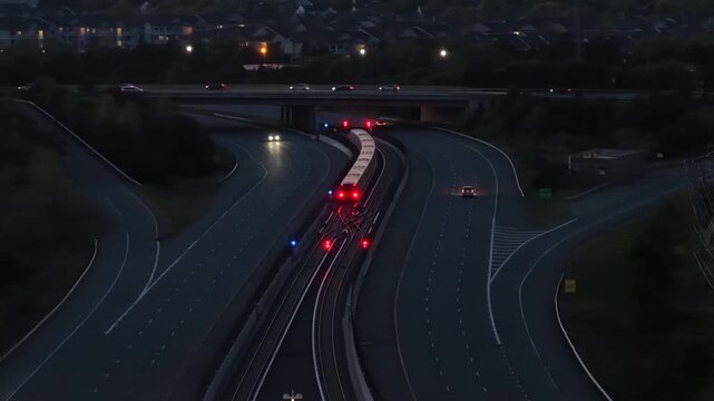 Aerial wide shot of Ashburn, Virginia highway at night with metro train running through center, illuminated by car headlights and urban lights in modern suburban transportation scene. USA at dusk. 