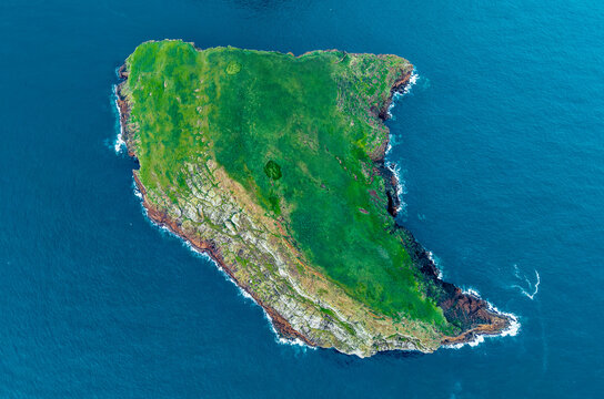 Aerial view of the rugged, verdant islet of Ilheus das Cabras embraced by the deep blue Atlantic, a jewel of nature, Terceira, Azores, Portugal.